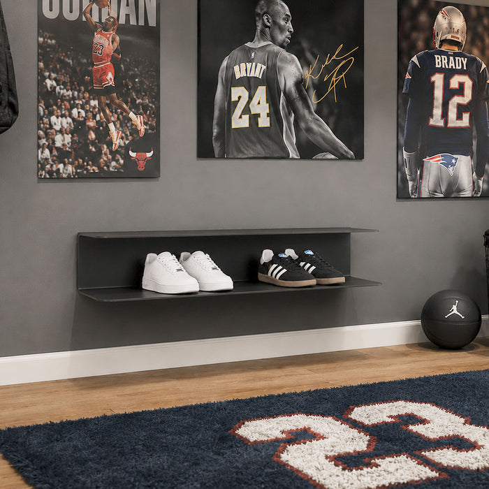 Chuck It Up Shoe Rack wall-mounted in black steel with two straight shelves holding sneakers, displayed in a sports-themed room with hardwood floor and sports memorabilia.