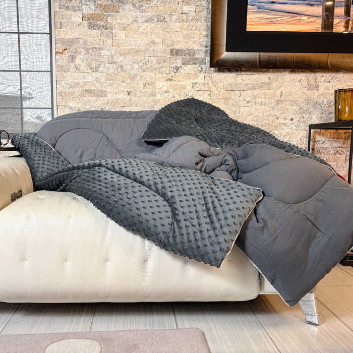 Gray comforter draped over a beige sofa in a living room setting.