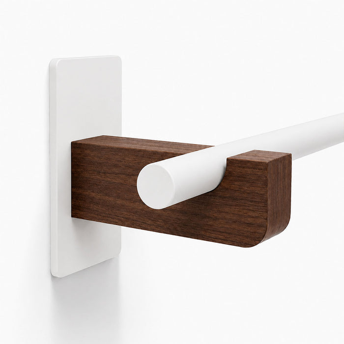 Close-up of a minimalist Draper Curtain Rod System featuring a white rod supported by a rich wood bracket mounted on a white wall.
