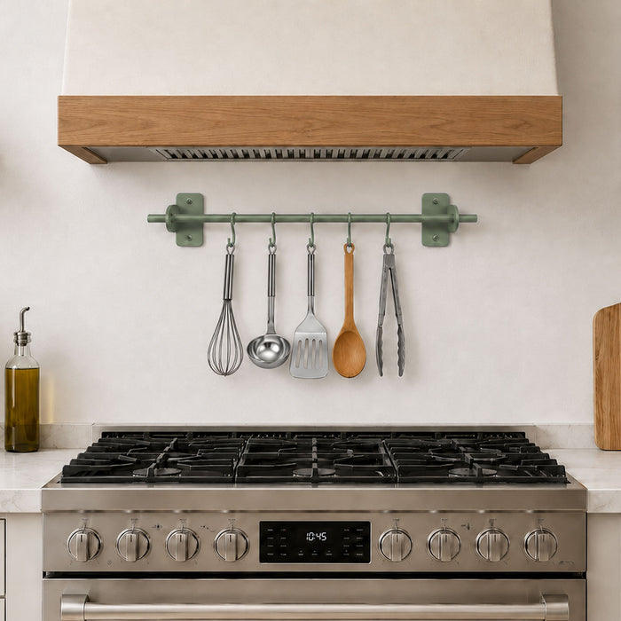 Etta Utensil Rack mounted on a kitchen wall above a stainless steel stove, holding metal and wooden cooking utensils in a minimalist, functional space.