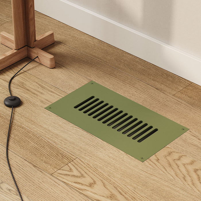 Felix Vent Cover in matte army green steel with horizontal slots, set flush in light hardwood floor near natural wood furniture leg and black cable.
