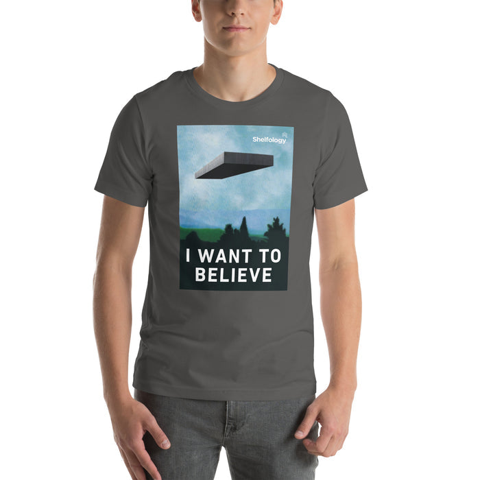 I Want to Believe T-shirt in dark gray featuring graphic of floating shelf over forest landscape with bold white text