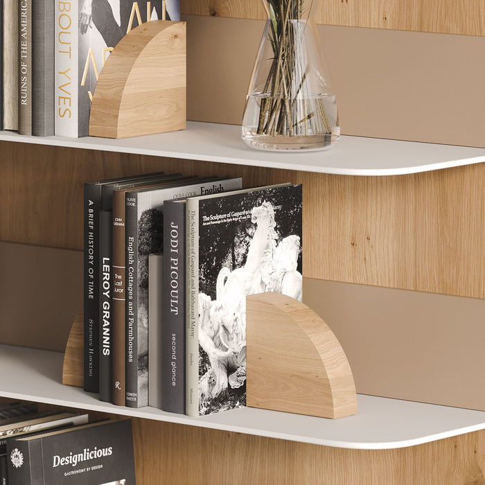 Image of a wall with two white tromso radius shelves, holding books and a vase. Three Maggie Radius (white oakd finish) bookends are positioned holding the books.
