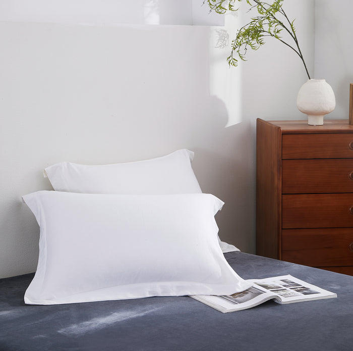 White pillows on a bed with a wooden dresser and plant in the background