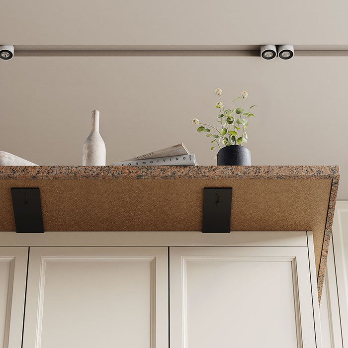 Otto Countertop Bracket in matte black steel providing strong, minimalist support for a granite countertop with decorative accents above white cabinetry.