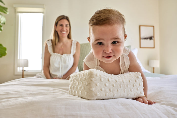 Baby lying on a bowroo nursing pillow  with a woman sitting in the background
